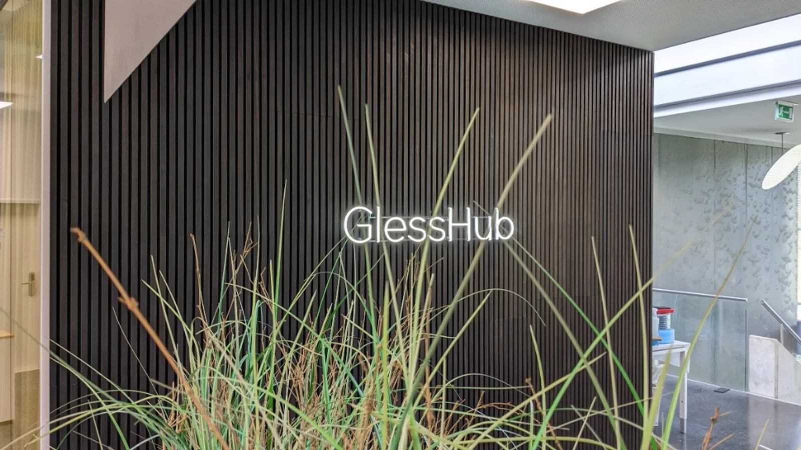 GlessHub-Leuchtschrift im Coworking-Bereich mit vertikaler Holzwand und Ziergräsern im Vordergrund