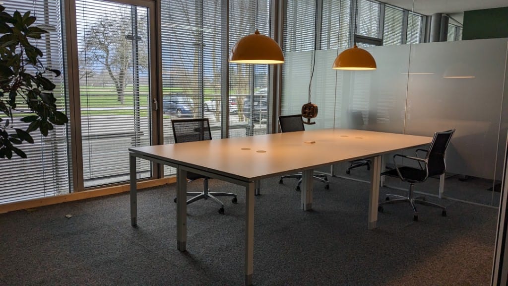FlexDesk im GlessHub: großer heller Schreibtisch mit ergonomischen Stühlen und gelben Pendelleuchten vor der Fensterfront